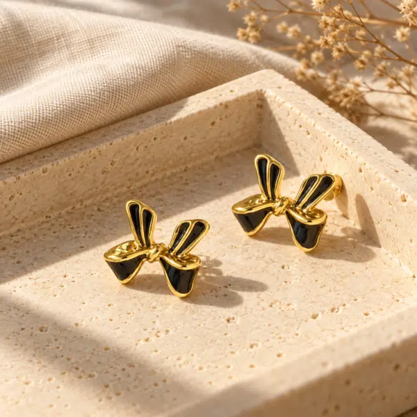 A pair of elegant black enamel bow gold plated earrings on a white background